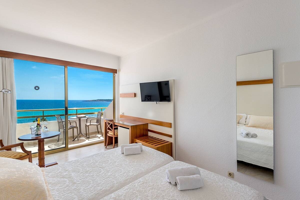 A hotel room with a balcony, a desk, a bed, and a TV.