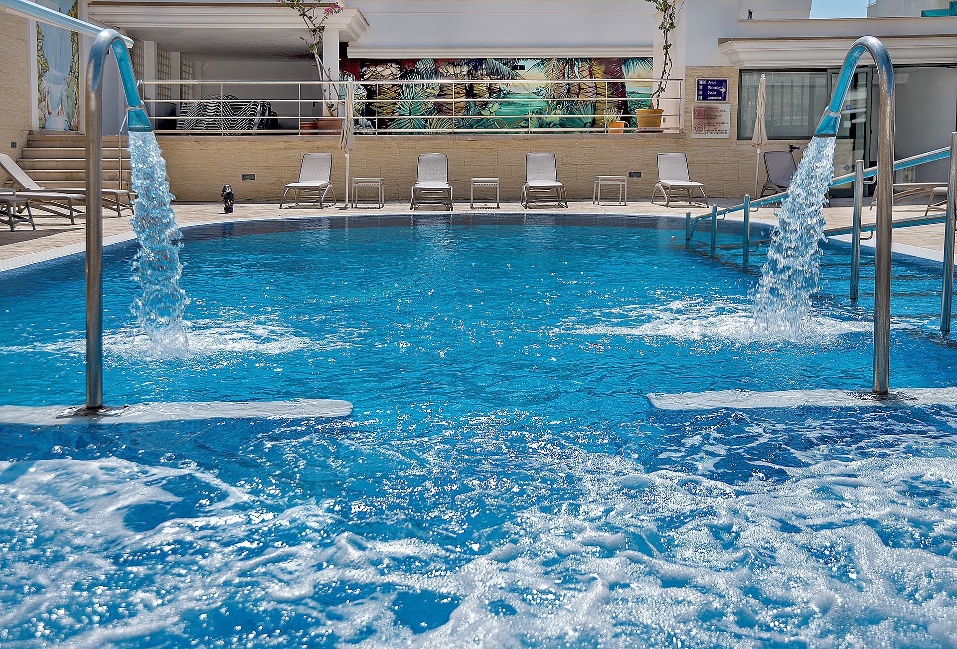 A swimming pool with water jets, lounge chairs, and a mural on the wall.