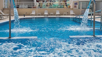 Una piscina con chorros de agua, sillas de descanso y un mural en la pared.