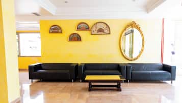 A lobby with a yellow wall, three black sofas, a wooden coffee table, and a large mirror.