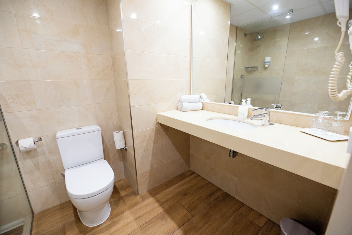 A bathroom with a toilet, sink, mirror, and shower.