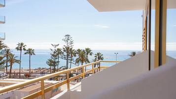 A balcony with a view of the beach, palm trees, and the ocean.