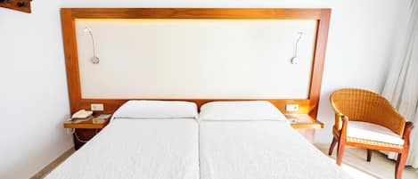 Una cama doble con cabecera de madera, una mesita de noche con un teléfono y una silla de mimbre.