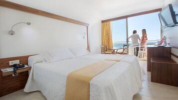 Habitación de hotel con cama, escritorio, silla, televisor y balcón con vistas.