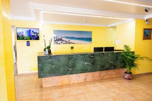 A reception desk with a marble top, a large framed beach photograph, a potted plant, and a security camera on the ceiling. - Biniamar (Sant Llorenc des Cardassar)