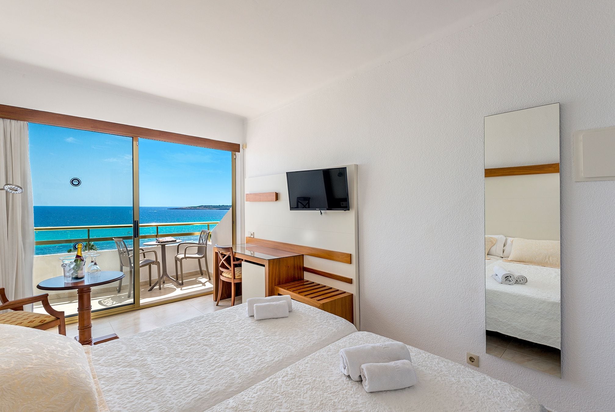A hotel room with a balcony, a desk, a bed, and a TV.