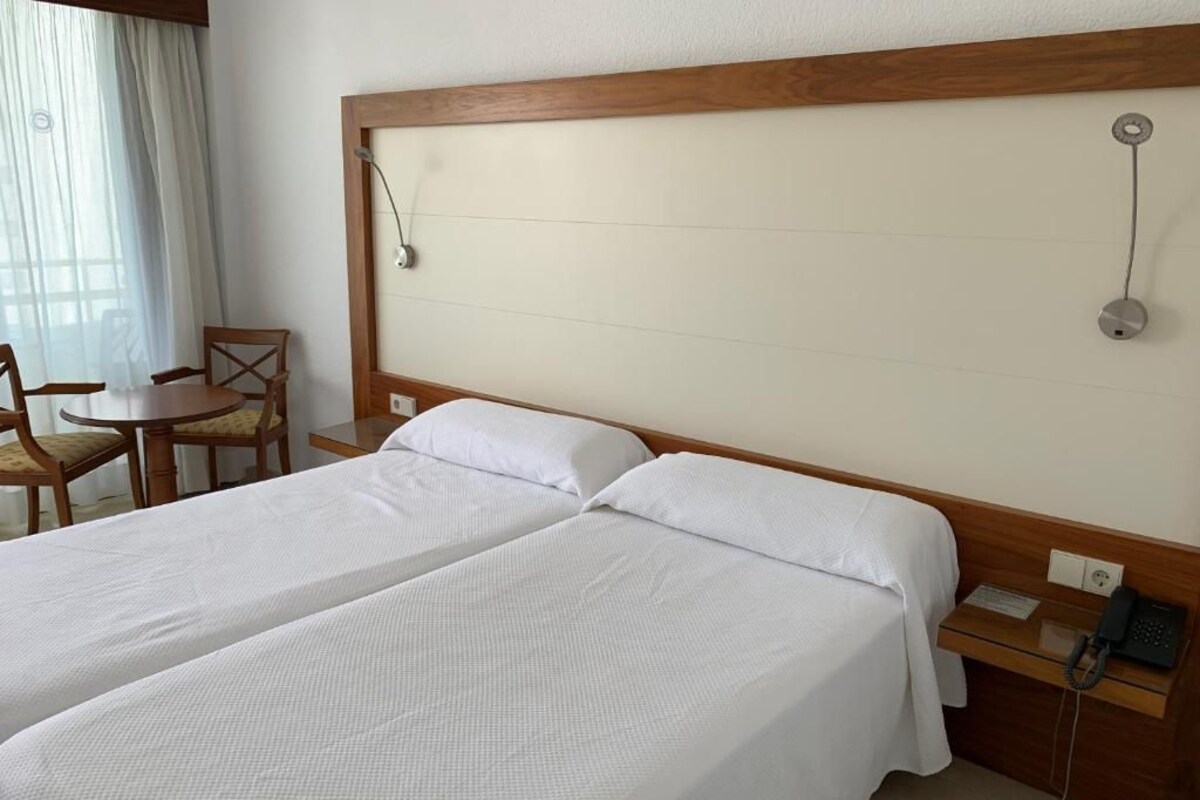 A hotel room with two single beds, a wooden headboard, a desk with a telephone, and a chair.