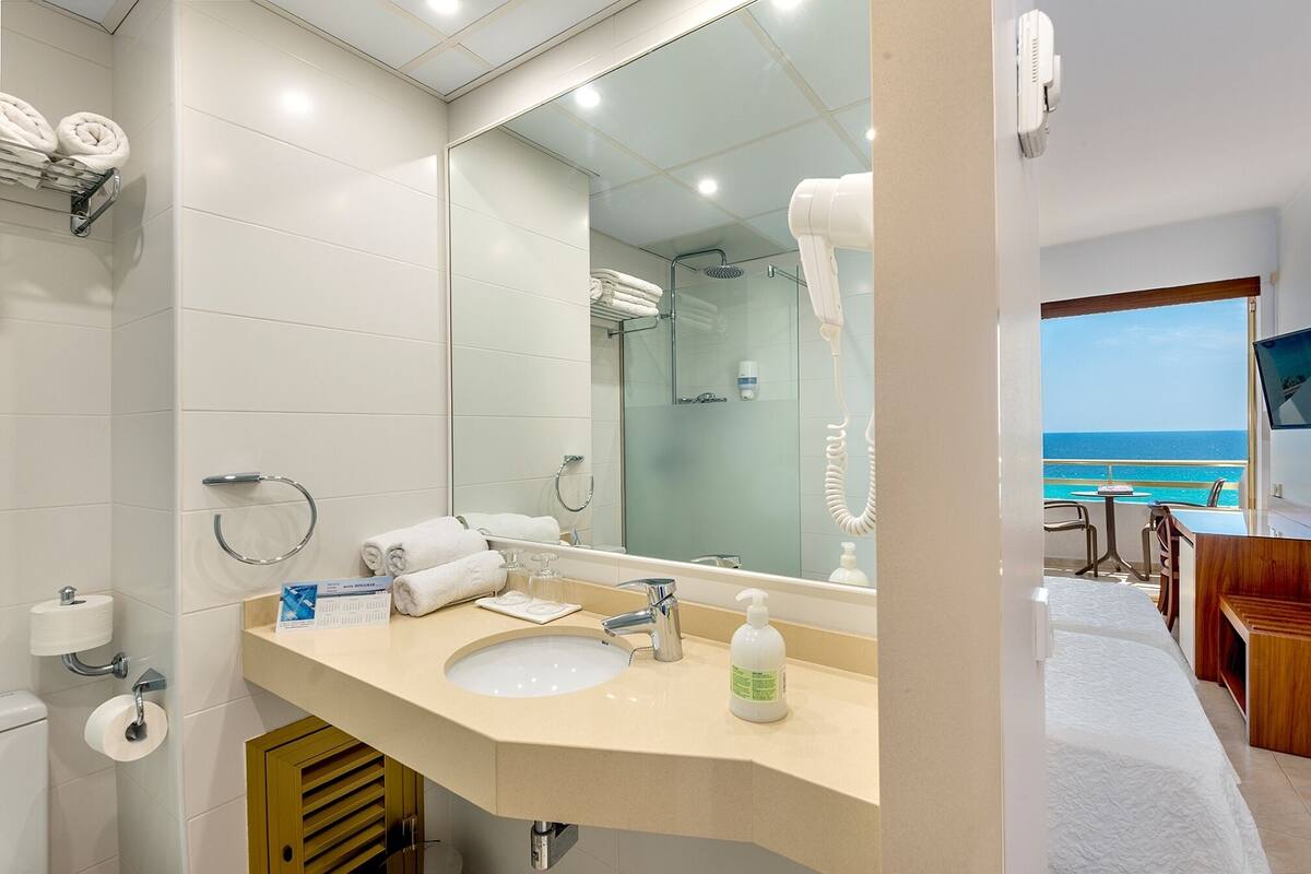 A hotel bathroom with a sink, mirror, and toiletries. There is a view of the ocean through the window.
