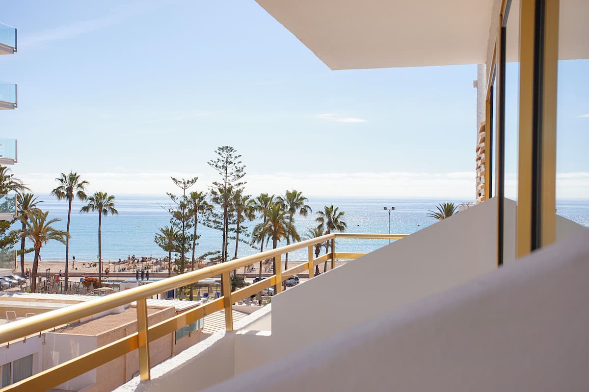 A balcony with a view of the beach, palm trees, and the ocean.