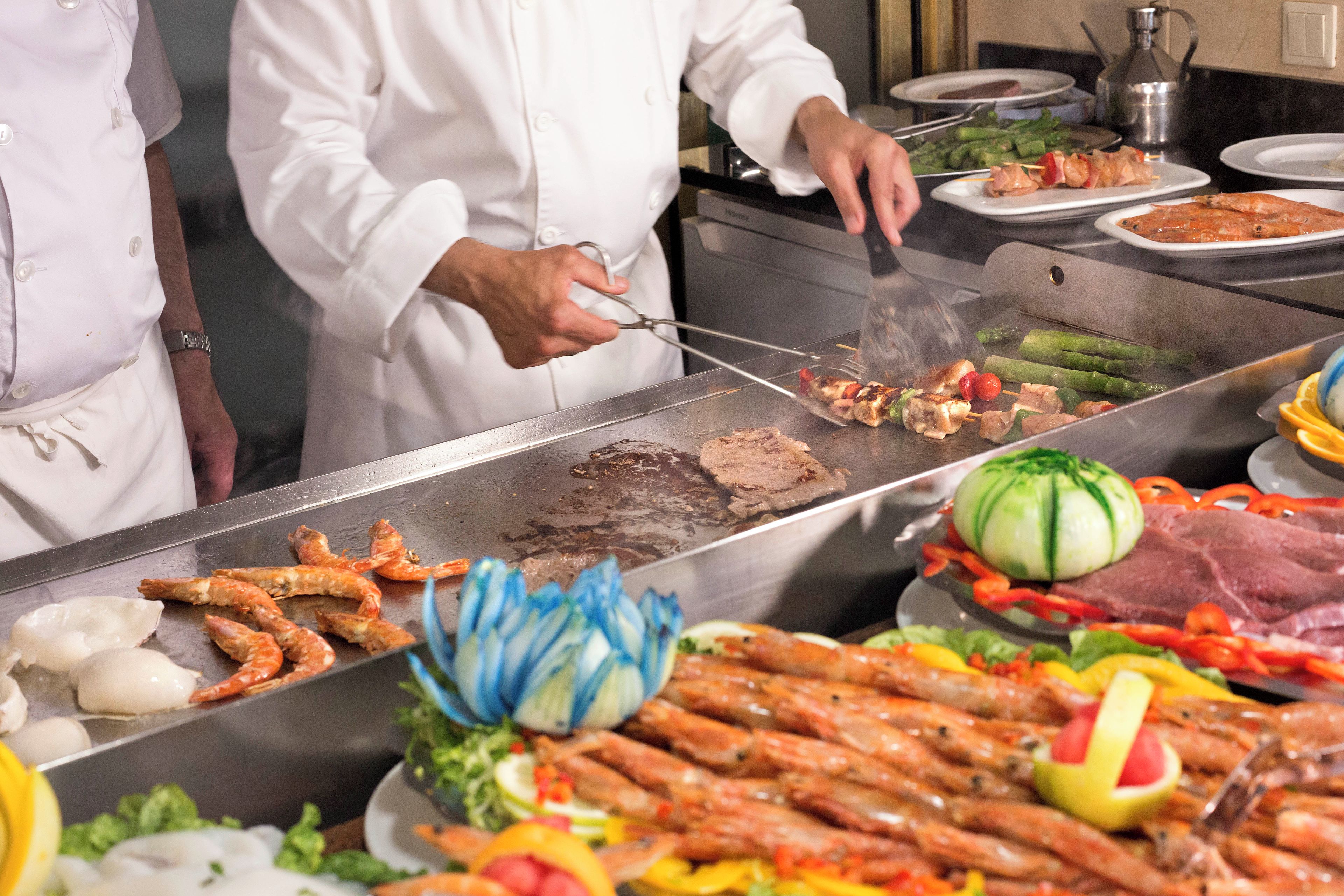 A chef preparing food on a grill with various meats and vegetables.