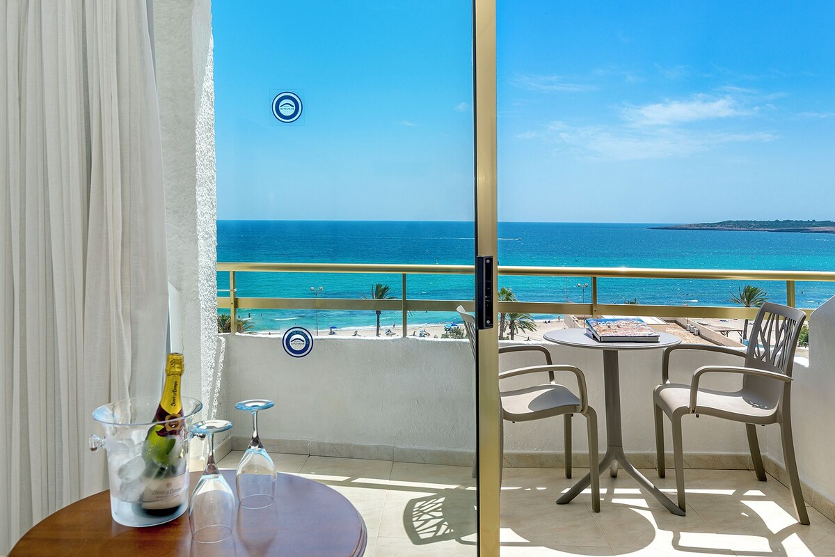 A balcony with a view of the sea, a table with chairs, and a bottle of champagne.