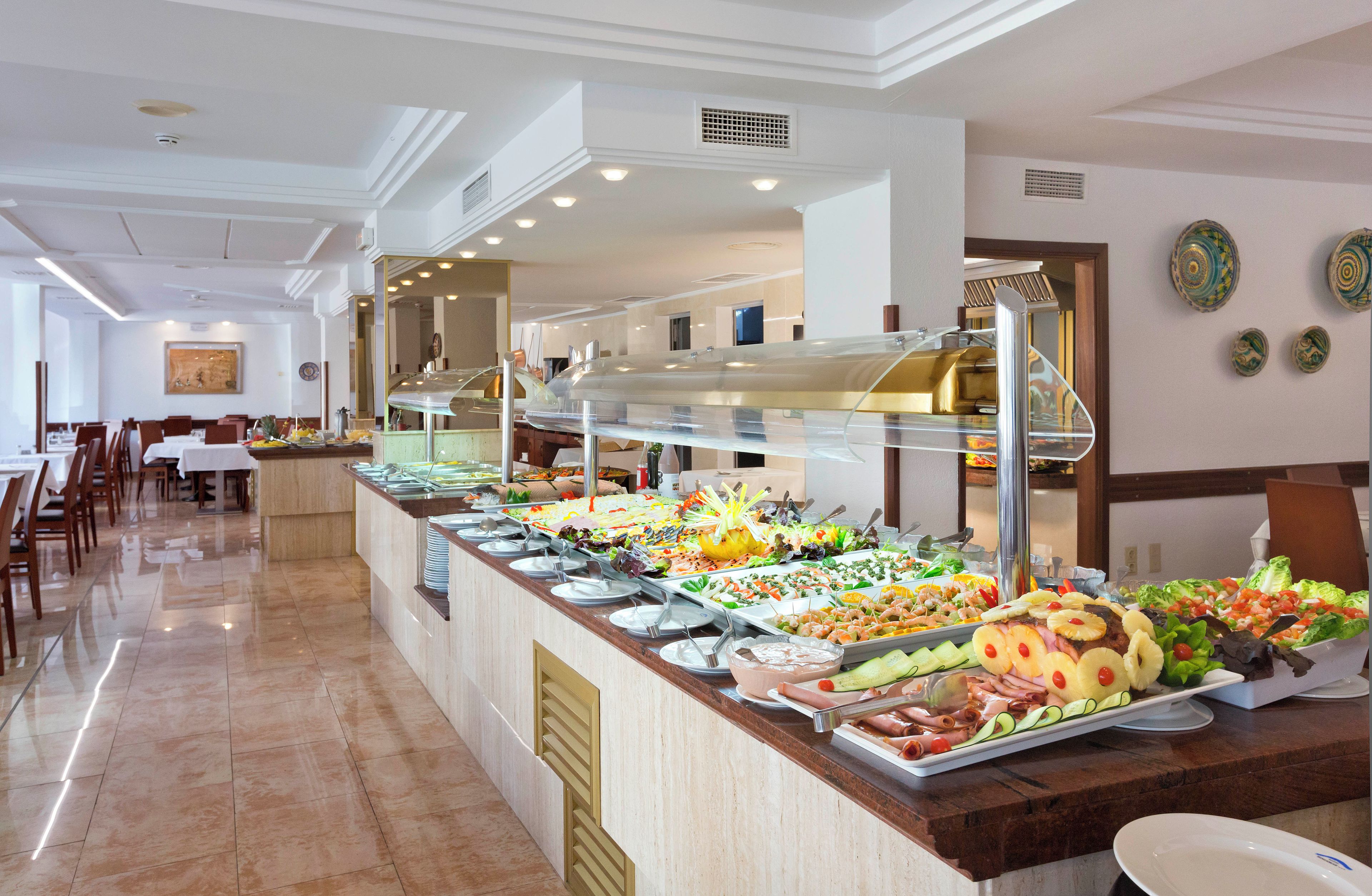 A buffet with various food options, a seating area with tables and chairs, and a ceiling with recessed lighting.