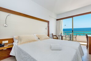 A hotel room with a large bed, a bedside table, a chair, a small table with a bottle, and a view of the sea. - Biniamar (Sant Llorenc des Cardassar)