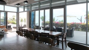 Un vaste espace dédié à la salle à manger, avec une longue table en bois et des chaises, de grandes fenêtres offrant une vue sur un patio aménagé avec du mobilier d’extérieur et des plantes.