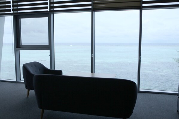 A room with large windows offering a view of the sea. There are two chairs and a table. - Saipan IRIS Pool Villa (Saipan)