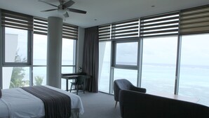 Une chambre d’hôtel équipée d’un lit, d’un bureau, d’une chaise et de grandes fenêtres donnant sur la mer.