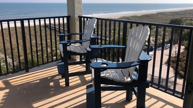 Ein Balkon mit zwei Adirondack-Stühlen mit Blick auf einen Strand.