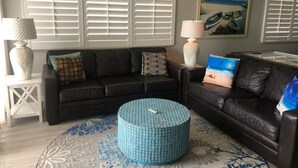 Ein Wohnzimmer mit zwei dunklen Ledersofas, einem blauen runden Ottomanen und einem gemusterten Teppich.