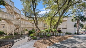 A multi-story building with a central courtyard, outdoor seating area, and a staircase leading to the upper floors. - The Ocean Bridge C34 - Beautiful Unit Across from Beach (Myrtle Beach)