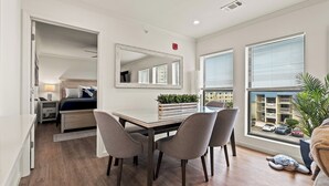 A modern bedroom with a bed, bedside table, lamp, and a view of the city through large windows. - The Ocean Bridge C34 - Beautiful Unit Across from Beach (Myrtle Beach)