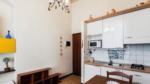A compact kitchen with white cabinets, a microwave, and a sink. There's a wooden bench and a dining table with a decorative bowl. - Grimaldi 8 Apartment by Wonderful Italy (Catania)