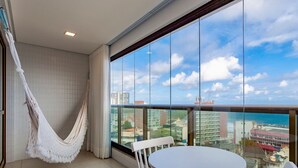 Un balcón con una mesa y sillas blancas, una hamaca blanca y vistas a la ciudad y al océano.
