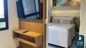 Una habitación de hotel moderna con un televisor de pantalla plana montado en una pared de paneles de madera, una cama con ropa blanca y un cuadro de un paisaje urbano.