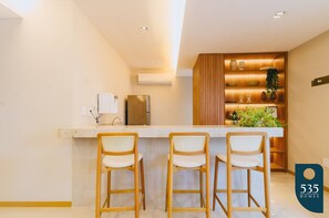 A modern kitchen with a bar area, two bar stools, and a wooden cabinet with decorative items. - Beautiful Bedsitter Apartment in Salvador (Salvador)