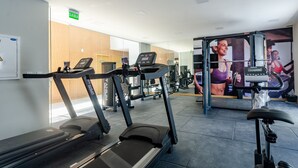 Un gimnasio con cintas de correr, máquinas de pesas y un espejo grande.