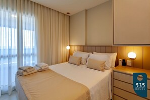 Hotellihuone, jossa on sänky, yöpöydät, pieni sivupöytä ja suuri ikkuna, jossa on verhot.