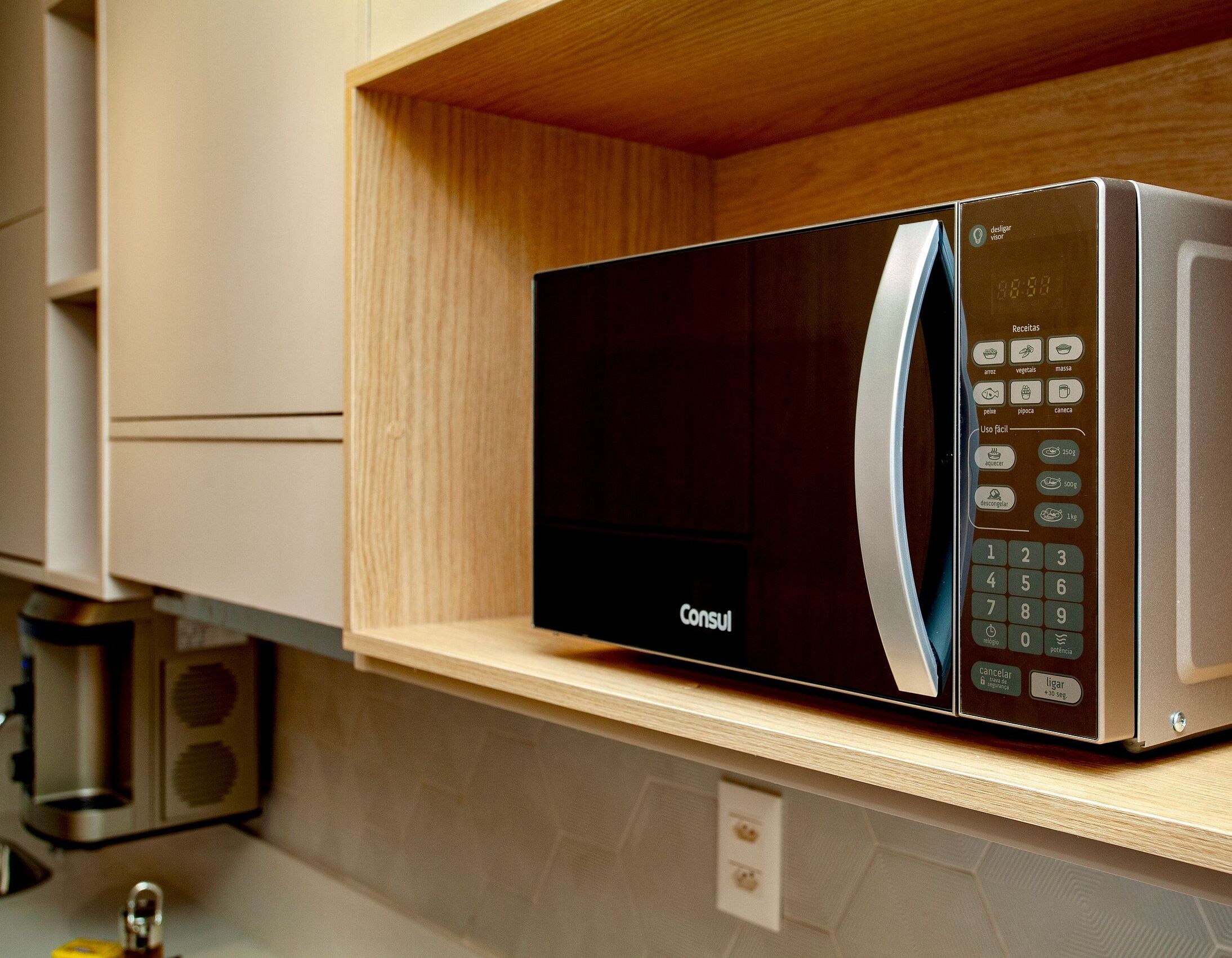 A modern kitchen with a built-in microwave on a wooden shelf.