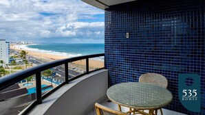 Un balcón con vista a la playa y al océano, una mesa redonda y sillas de mimbre.
