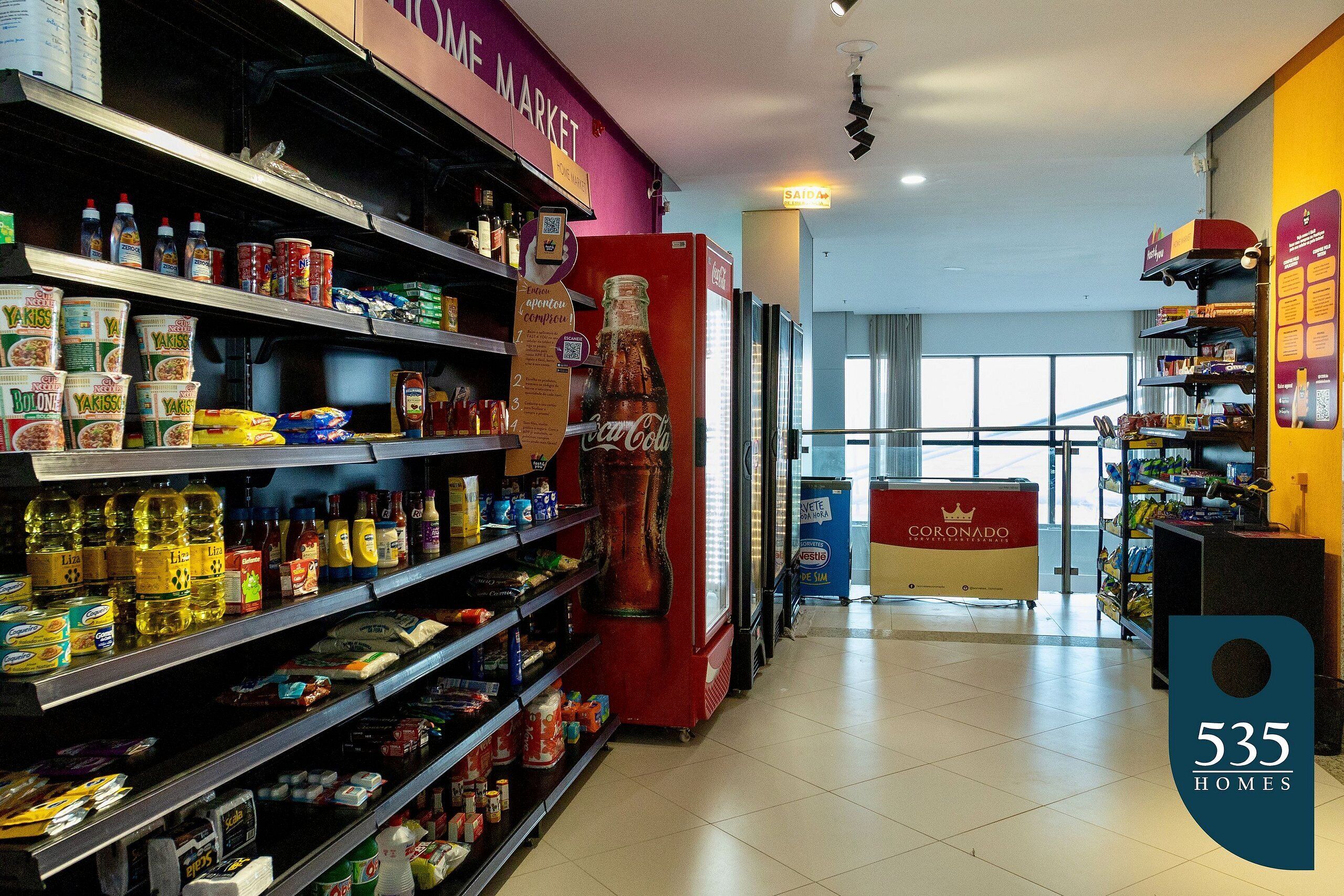 A grocery store interior with shelves stocked with various food items, a refrigerator, and a sign indicating '535 HOMES'.