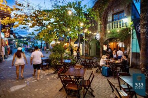 An outdoor café with tables and chairs, surrounded by buildings and greenery.