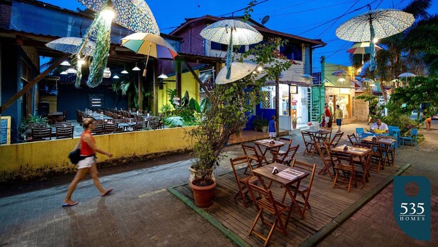 An outdoor dining area with wooden tables and chairs, surrounded by umbrellas. - Apartment in Itacaré: Sun, Sea, and Comfort (Itacaré)