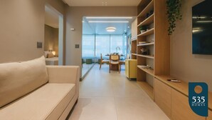 Una sala de estar moderna con un sofá, una zona de comedor con una mesa y sillas, y una cocina con mostrador y estanterías.