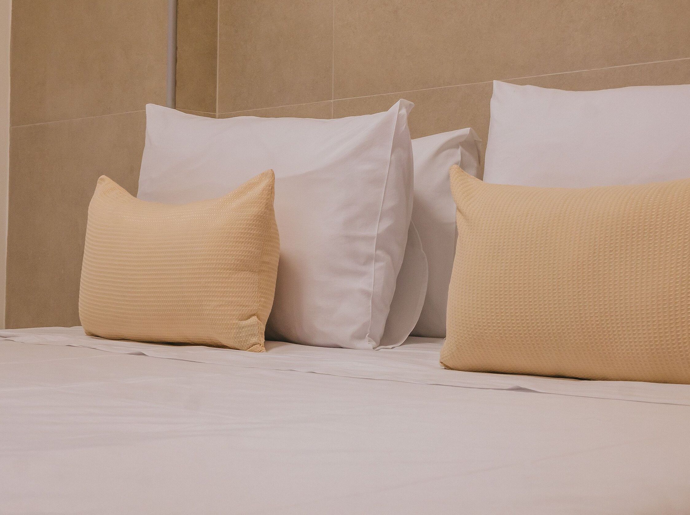 Una cama con ropa de cama blanca y tres almohadas en diferentes tonos de beige.