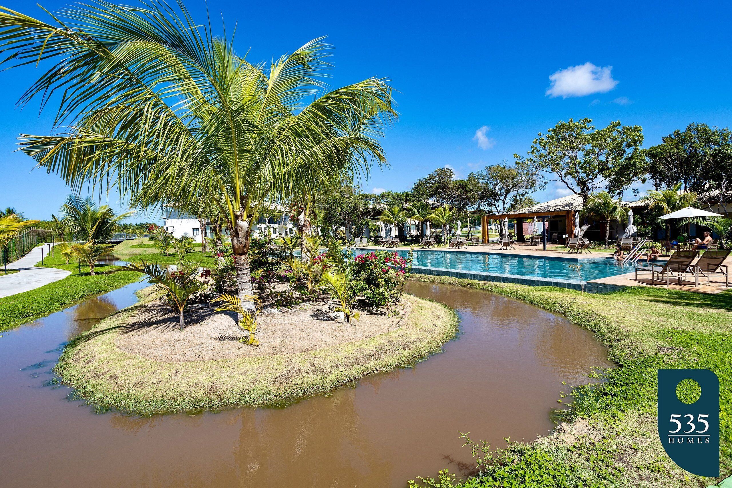 A pool area with palm trees, a small island, and a clear blue sky.
