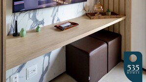 Un salon moderne doté d’un grand téléviseur à écran plat fixé sur un mur en marbre, d’une étagère en bois ornée d’objets décoratifs et d’un banc en cuir marron.