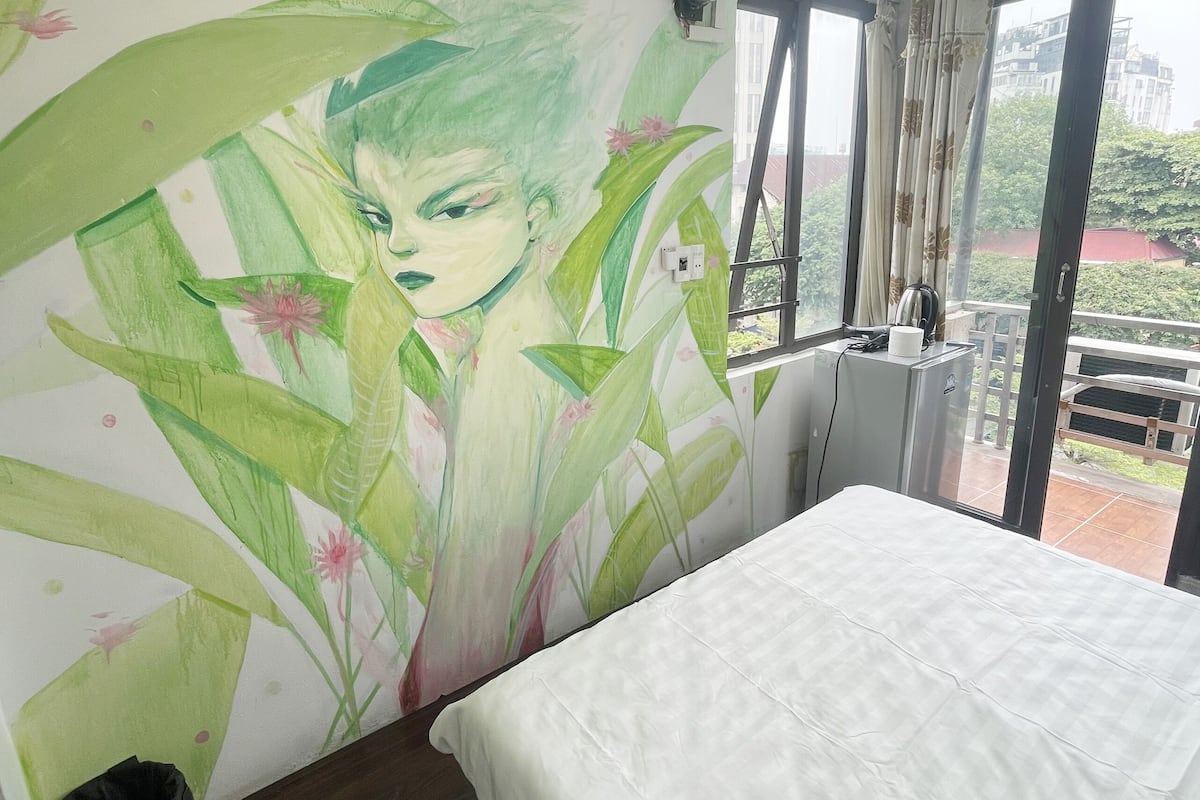 A hotel room with a bed, a wall mural, a window with curtains, and a balcony.