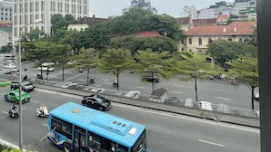 A city street with a blue bus, buildings, and trees. - Red River Homestay (Hanoi)