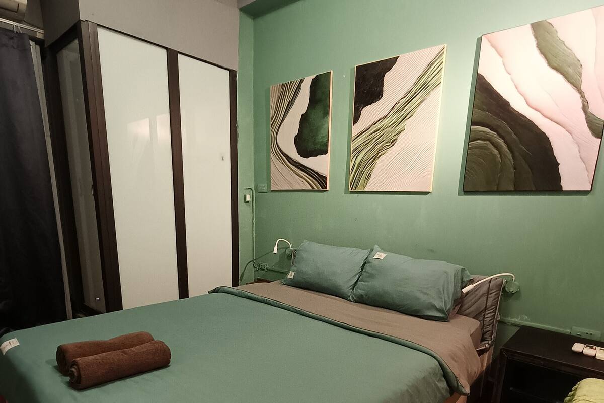 A bedroom with a bed, a nightstand, a wardrobe, and artwork on the wall.