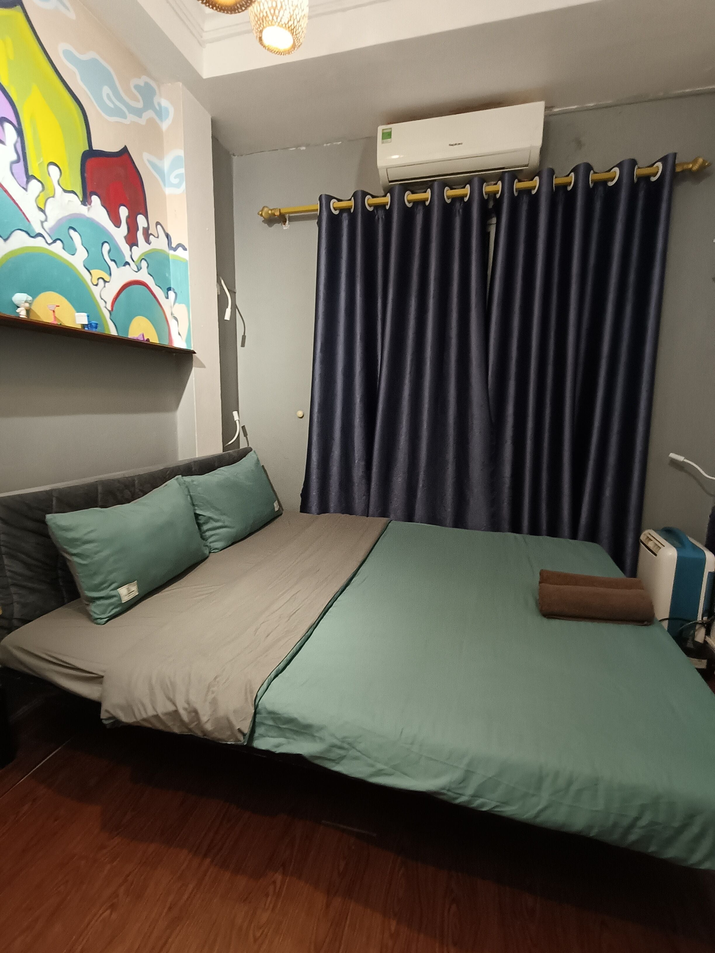 Una camera da letto con un letto, un condizionatore d'aria a parete, una tenda e un murale colorato.