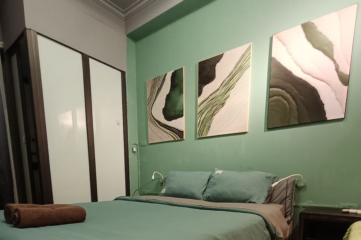 A bedroom with a bed, green walls, and artwork.