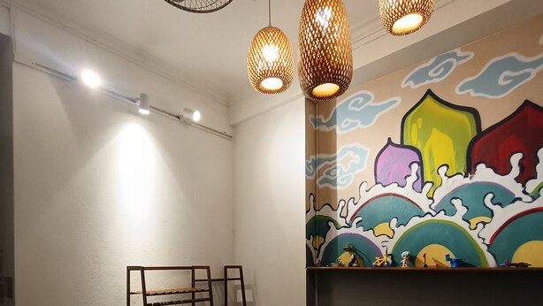 A bedroom with a bed, a wall-mounted shelf, a standing fan, and a colorful mural. - Red River Homestay (Hanoi)
