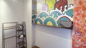 A room with a wooden bench, a metal shelf with a kettle, a coffee maker, and a colorful mural on the wall. - Red River Homestay (Hanoi)