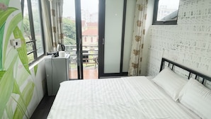 A bedroom with a bed, a small kitchenette, and a balcony with a view of buildings. - Red River Homestay (Hanoi)