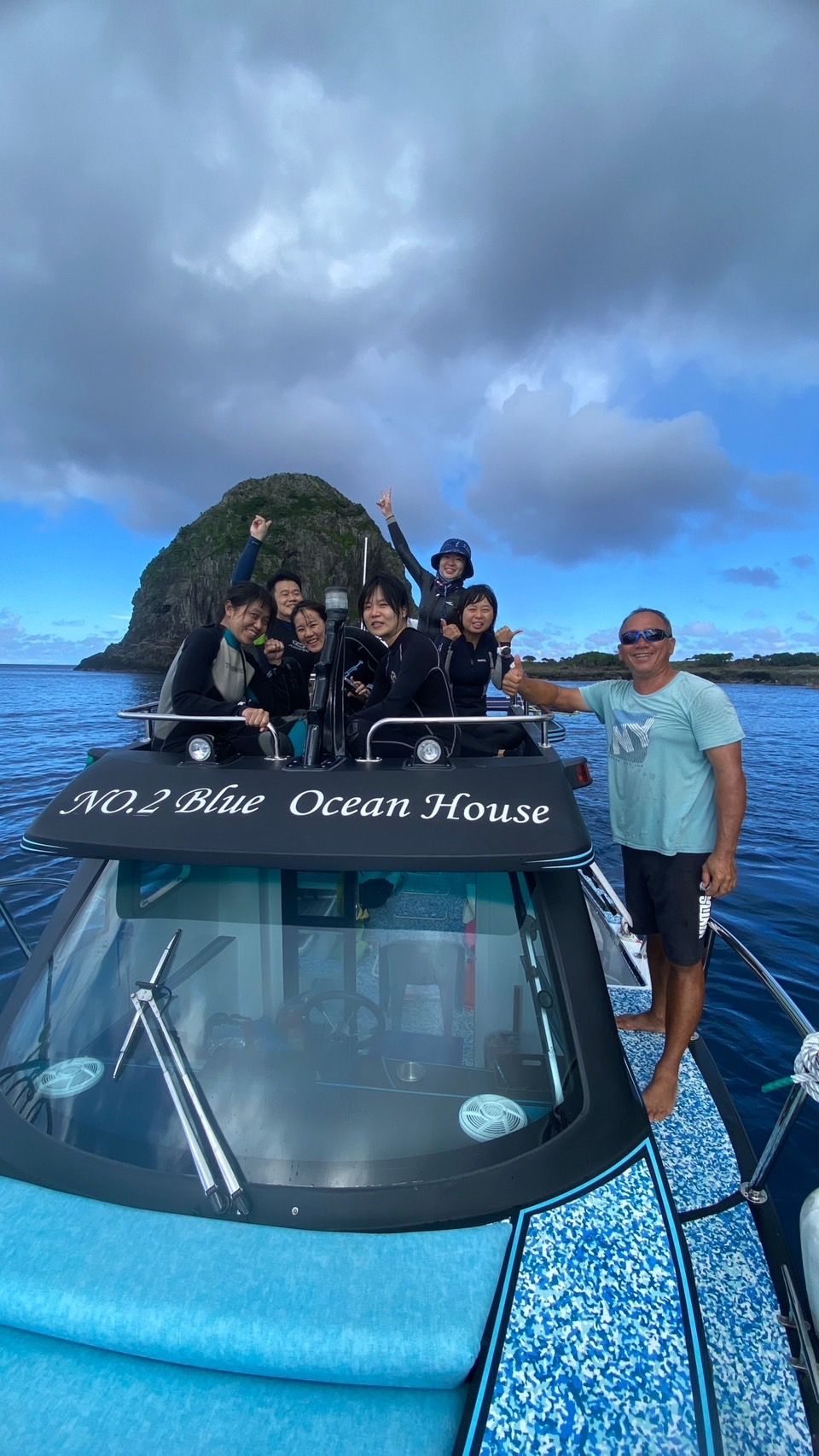 A boat with the text 'NO.2 Blue Ocean House' on the deck, passengers on board, and a mountainous island in the background.