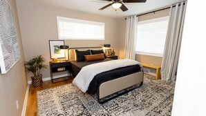 A bedroom with a bed, bedside tables, a ceiling fan, and a large window with curtains. - New - Spacious 4B2B House in Tech Terrace (Lubbock)