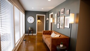A hallway with a brown leather sofa, a clock, and framed artwork on the walls. - New - Spacious 4B2B House in Tech Terrace (Lubbock)